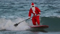 Siap untuk menyambut Natal dan menyebarkan suka cita Santa memilih berselancar menggunakan papan seluncur di Pantai Florida, Amerika Serikat. Joe Raedle/Getty Images