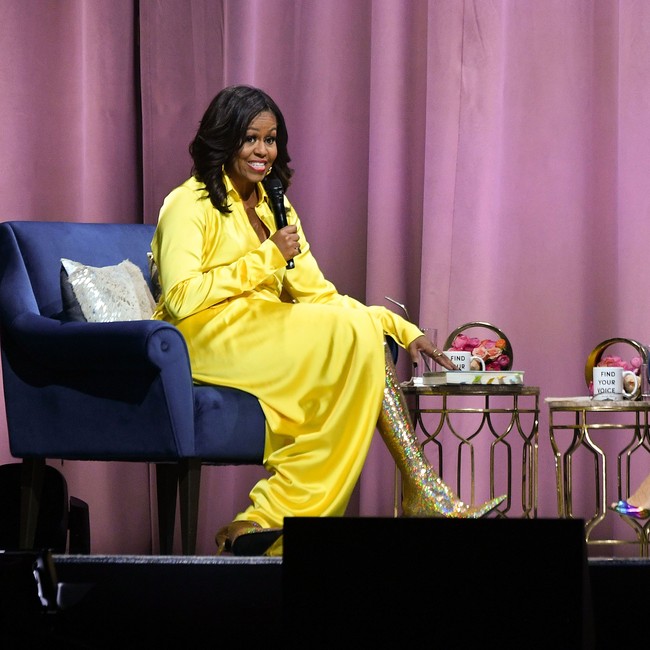 Michelle Obama memilih boots tinggi glitter warna kuning emas berkilauan. Boots setinggi paha itu dia padukan bersama blouse dan rok high-slit kuning satin silk. Foto: Dia Dipasupil/Getty Images