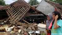 Nampak warga melewati sebuah rumah yang rusak parah dan sebuah mobil nampak menabrak puing-puing bangunan tersebut.
