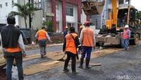 Puluhan petugas dari Linmas, Satpol PP Kota Surabaya dan Dinas PU Bina Marga masih melakukan upaya pengeringan jalan yang baru diaspal dengan cara sederhana, yaitu memakai karung goni dan compressor.