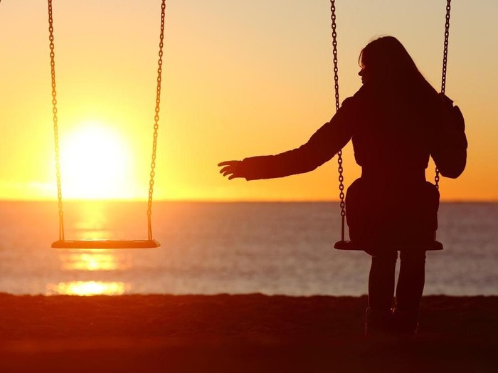 Single or divorced woman alone missing a boyfriend while swinging on the beach at sunset
