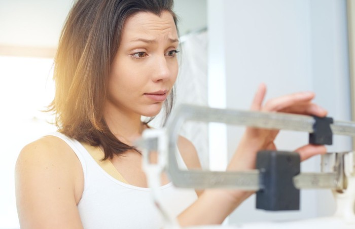 diet timbangan resolusi sehat Shot of a young woman weighing herself on a scale