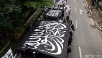 Dengan membawa bendera kalimat tauhid dan spanduk, mereka berjejer hampir memenuhi Jalan Mayjen Sungkono mulai dari depan Bank Mualamat hingga Jembatan penyebarangan depan Vida.