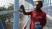 Pekerja tengah mengecat pagar pengaman JPO.
