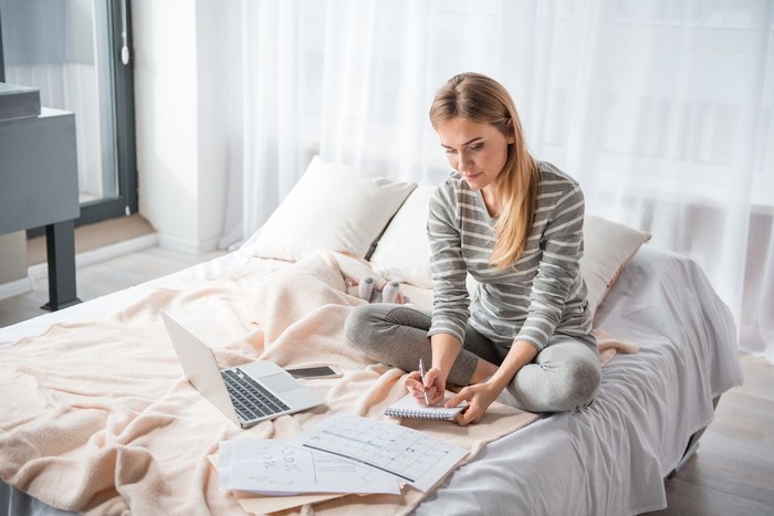 ilustrasi ibu Calm woman sitting on bed and making notes into notepad while baby is sleeping. She is looking concentrated