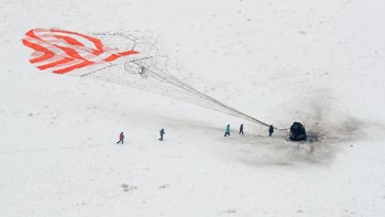 Tim penyelamat yang dibawa helikopter segera mendatangi kapsul yang tampak hangus tersebut dan mendarat dengan bantuan parasut besar. Foto: Reuters