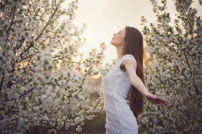 Portrait of a beautiful young woman enjoying spring among trees in bloom.