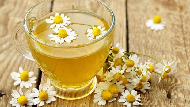 Herbal tea with lemon slice on a white wooden table with chamomile plants and cinnamon.