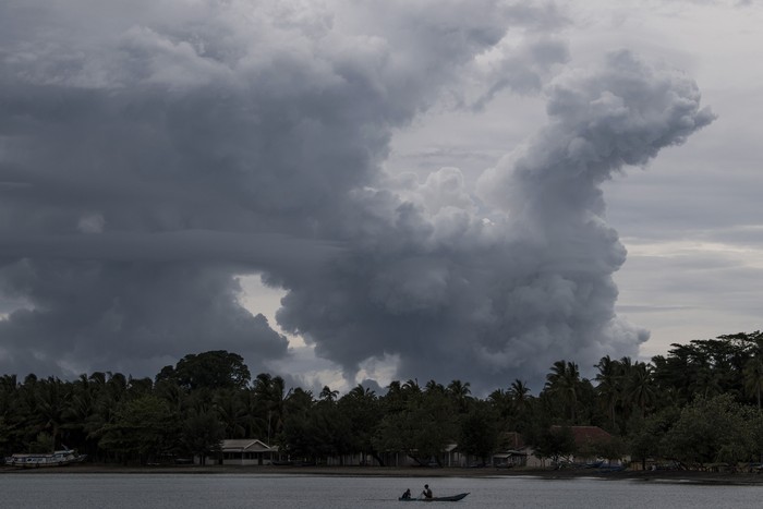 Warga mendayung sampan dengan latar belakang erupsi Gunung Anak Krakatau di Pelabuhan Pulau Sebesi, Lampung Selatan, Lampung, Selasa (1/1/2019). Pusat Vulkanologi dan Mitigasi Bencana Geologi menyatakan Gunung Anak Krakatau masih berada di level III (Siaga). ANTARA FOTO/Sigid Kurniawan/wsj.