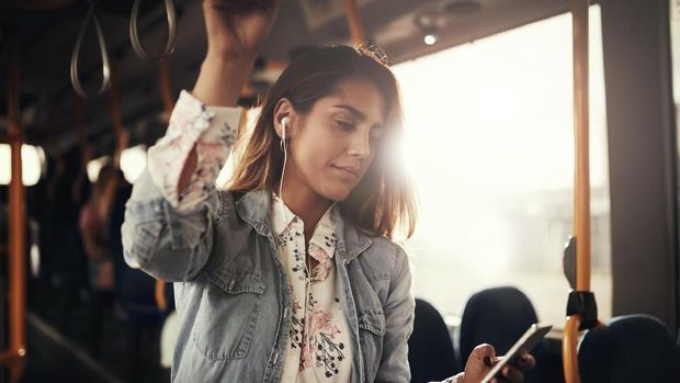 Young woman smiling while riding on a bus listening to music on a smartphone