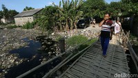 Seorang warga melintasi jembatan yang di bawahnya dipenuhi oleh tumpukan sampah yang berbau menyengat, Senin (7/1/2019).
