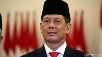 Doni tampak mengenakan setelan jas warna hitam dan peci warna hitam.