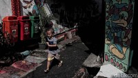 Seorang anak berjalan di gang yang kini penuh mural tersebut.