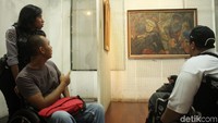 Dua orang penyandang disabilitas melihat-lihat lukisan yang dipajang di museum.