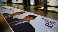 Di spanduk itu Jokowi dan Maruf Amin tampak mengenakan kemeja warna putih serta peci hitam. Sementara Prabowo-Sandiaga mengenakan setelan jas. Mereka juga mengenakan peci warna hitam.