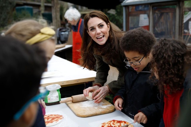 Ia sempat membuat pizza bersama para murid dari SD yang berada di sekitaran lokasi tersebut. Mendapat pertanyaan dari anak-anak bilamana Ratu Elizabeth II suka makan pizza, Kate pun menjawab, Itu pertanyaan yang bagus tapi aku tidak tahu. Nanti aku tanyakan ke Ratu, jawab Kate. (Foto: Getty Images)