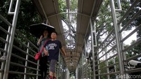 Seorang pejalan kaki melintasi jembatan penyeberangan orang (JPO) di Jalan Merdeka Barat, dengan menggunakan payung akibat atap JPO bolong, Jakarta, Jumat (18/1/2019).