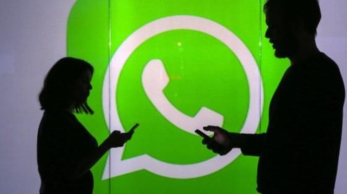 People are seen as silhouettes as they check mobile devices whilst standing against an illuminated wall bearing WhatsApp Incs logo in this arranged photograph in London, U.K., on Tuesday, Jan. 5, 2016. WhatsApp Inc. offers a cross-platform mobile messaging application that allows users to exchange messages. Photographer: Chris Ratcliffe/Bloomberg via Getty Images