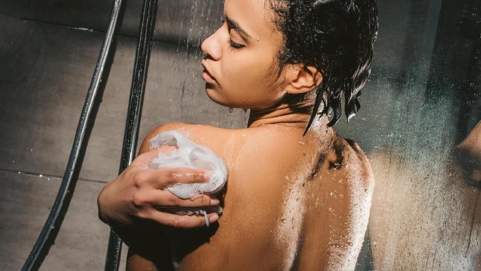 back view of attractive african american woman with sponge taking shower