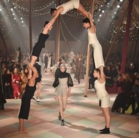 Para pemain akrobat membentuk formasi piramida yang menyimbolkan kekuatan seorang perempuan. Model dalam balutan gaun mini transparan berjalan di bawahnya. (Foto: Pascal Le Segretain/Getty Images For Christian Dior)