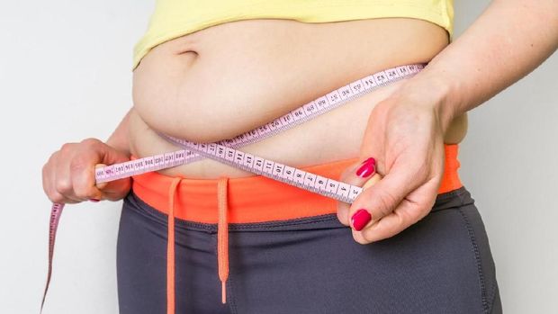 Overweight woman with tape is measuring fat on belly - obesity concept