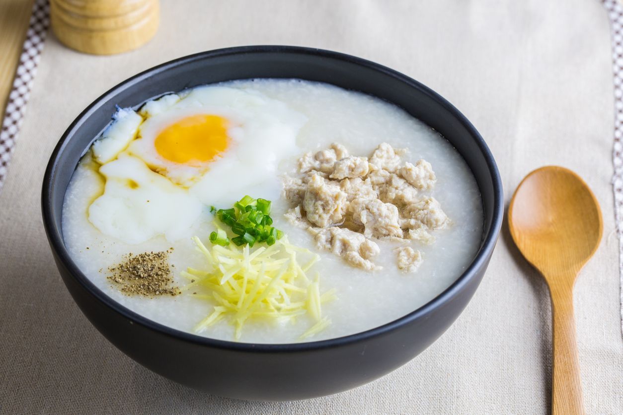 Close up to rice porridge is topping with ginger, spring onion, pepper, chicken, and onsen egg, Breakfast set on table, spoon, pepper grinder. breakfast in Asia call 