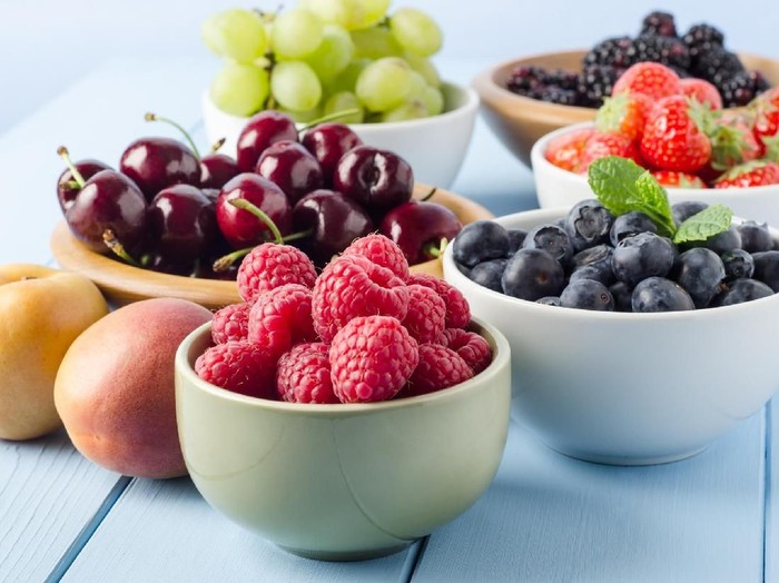 buah-buahan segar A selection of different Summer fruits, in a variety of bowls on a painted blue wood planked farmhouse kitchen table, against a light blue background.