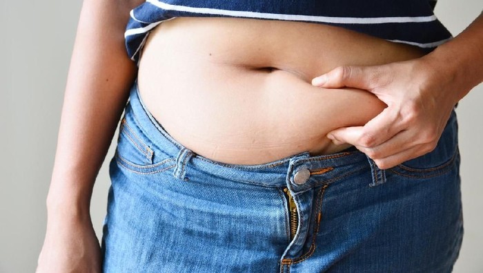 perut buncit Overweight woman with tape is measuring fat on belly - obesity concept
