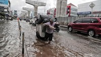 Seorang warga menarik gerobak penuh muatan di jalan yang terendam air setinggi lutut.