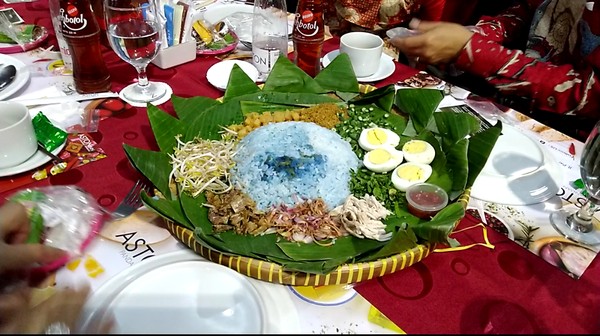 Hidangan utamanya berupa nasi warna biru dengan nama nasi ulam bunga telang, asimilasi peranakan Malaysia dan Singapura. Disajikan dengan wadah tampah dan dikelilingi srundeng, telur, gereh, satu tampah bisa dinikmati oleh 4 orang (Angling/detikTravel) Hidangan utamanya berupa nasi warna biru dengan nama nasi ulam bunga telang, asimilasi peranakan Malaysia dan Singapura. Disajikan dengan wadah tampah dan dikelilingi srundeng, telur, gereh, satu tampah bisa dinikmati oleh 4 orang (Angling/detikTravel)