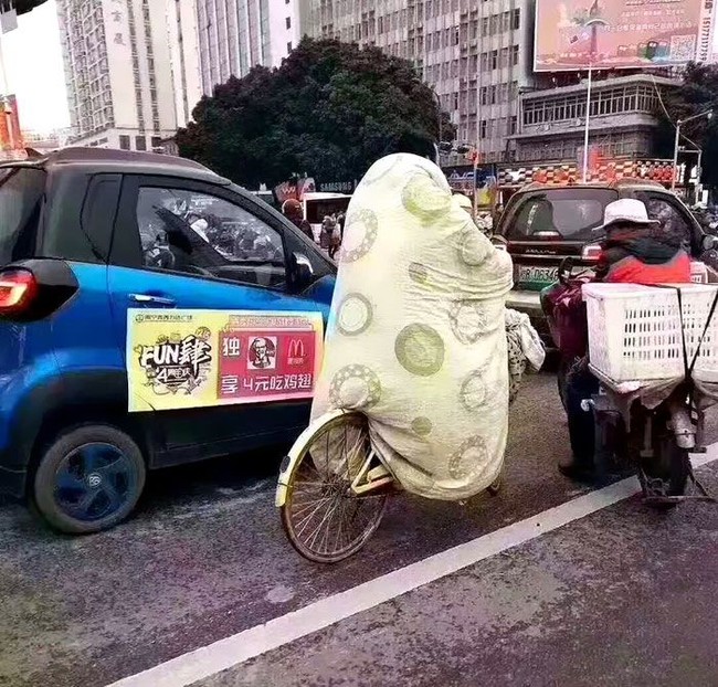 Ketika udara sedang dingin-dinginnya tapi kamu harus pergi dengan sepeda. Maka bersepeda sambil berselimut tebal menjadi solusi. Kenapa tidak? (Foto: Instagram/boredpanda)