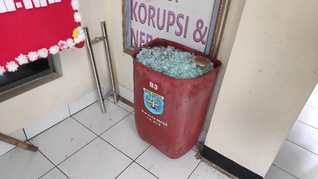 Sisa pecahan kaca pintu dimasukkan ke tempat sampah.
