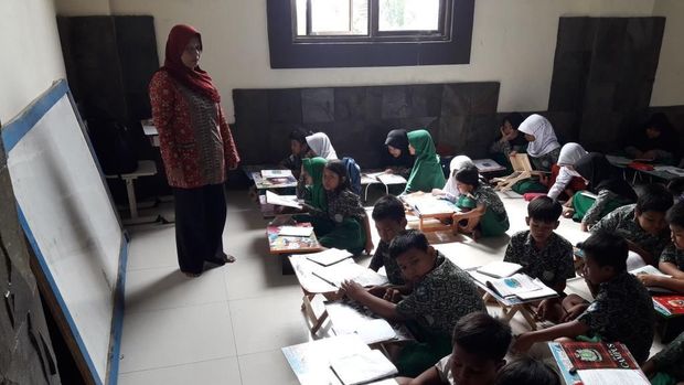 Guru mengajar dengan papan tulis yang disandarkan di dinding.
