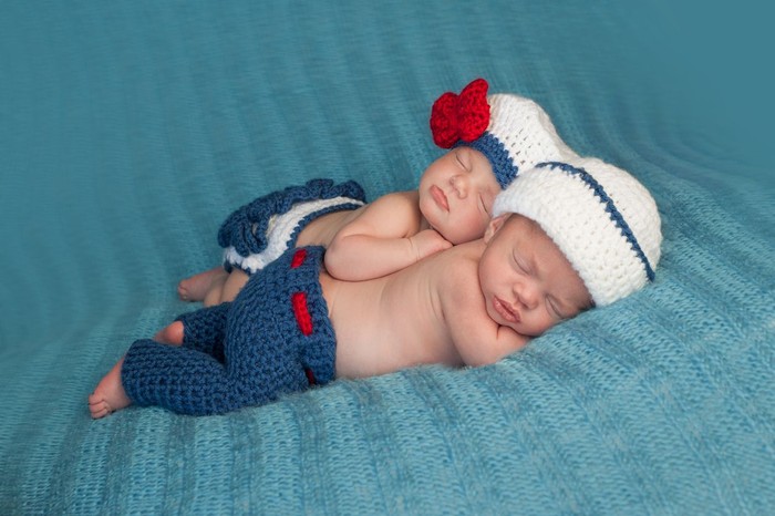 Ilustrasi bayi Five week old sleeping boy and girl fraternal twin newborn babies. They are wearing crocheted sailor outfits. One baby is lying on her stomach and the other is propped on top of her sister.
