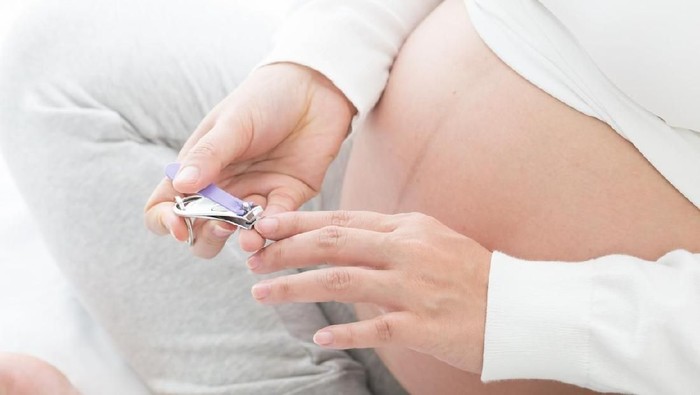 Pregnant woman cutting nails using nail clipper