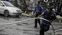 Dua orang petugas menarik selang air dari mobil pemadam kebakaran untuk membersihkan area di sekitar Gereja Katedral Jakarta.
