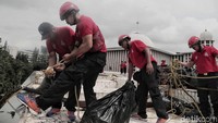 Para petugas bergotong-royong menurunkan sampah dari atap masjid.