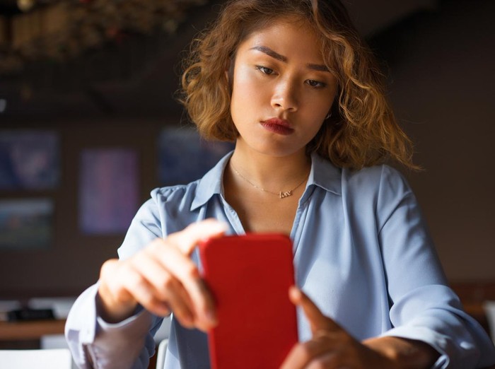 Closeup of thoughtful young Asian woman holding mobile phone and surfing Internet. Attractive student taking selfie at cafe. Communication and work balance concept