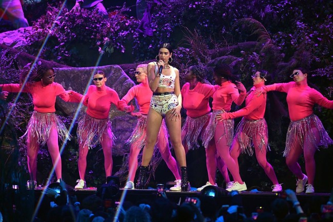 Dua Lipa lalu berganti pakaian. Kali ini mini dress biru bermotif bintang dengan aksen pita besar di belakang menjadi pilihannya. Untuk melengkapi gayanya, Dua mengandalkan anting berbentuk bintang. Foto: Getty Images