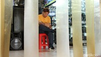 Pedagang menunggu pembeli dengan bermain smartphone di depan kiosnya.