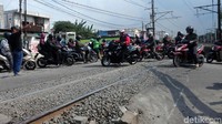 Saat kereta melintas, pemotor saling mendahuli melintasi rel kereta.