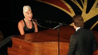 Lady Gaga menyanyi sambil memainkan piano, sementara Bradley duduk di depannya. REUTERS/Mike Blake