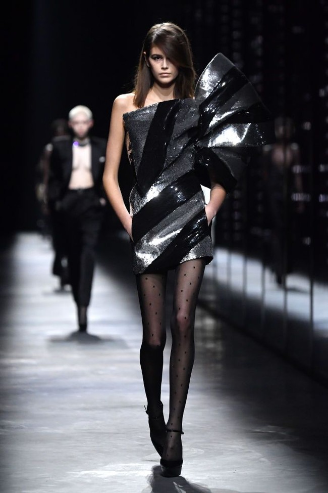 Look berikutnya menampilkan Kaia berbalut mini-dress metalik dengan aksen pita bervolume yang menutupi dada dan lengan kirinya. Rambut coklat alami Kaia kini dibiarkan tergerai bebas sehingga memancarkan kecantikan alami model 17 tahun itu. (Foto: Pascal Le Segretain/Getty Images)