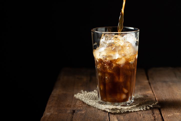 Ice coffee in a tall glass over and coffee beans on a old rustic wooden table. Cold summer drink on a dark background with copy space. The process of pouring drink from a coffee pot into a glass.