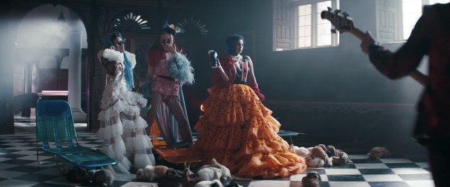 Priyanka Chopra memakai gaun ruffle dari Sensen Lii warna oranye, dengan babushka atau kerudung warna biru. Dia lalu menggantinya dengan gaun pink Giambattista Valli untuk mengendarai sepeda. Foto: Dok. YouTube/The Jonas Brother