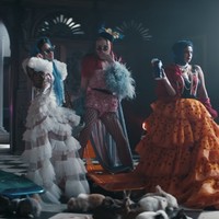 Priyanka Chopra memakai gaun ruffle dari Sensen Lii warna oranye, dengan babushka atau kerudung warna biru. Dia lalu menggantinya dengan gaun pink Giambattista Valli untuk mengendarai sepeda. Foto: Dok. YouTube/The Jonas Brother