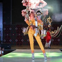 Memilih blus dan celana panjang serba oranye, Lycie Joanna asal Kepulauan Riau menyempurnakan gayanya dengan penutup mata bak superhero. Busananya juga dihiasi peralatan musik berwarna emas yang mempertegas karakter budaya Melayu di Riau.  Foto: Instagram/@officialputeriindonesia