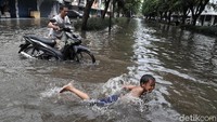 Seorang anak berenang mengadu kecepatan dengan sepeda motor yang mogok.