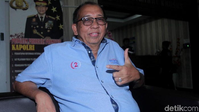 Mantan pebalap Alex Asmasoebrata memenuhi penggilan penyidik Polda Metro Jaya. Sambil tersenyum Alex melakukan pose salam dua jari.