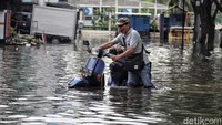 Tampak seorang warga tengah mendorong motor untuk menerobos banjir.